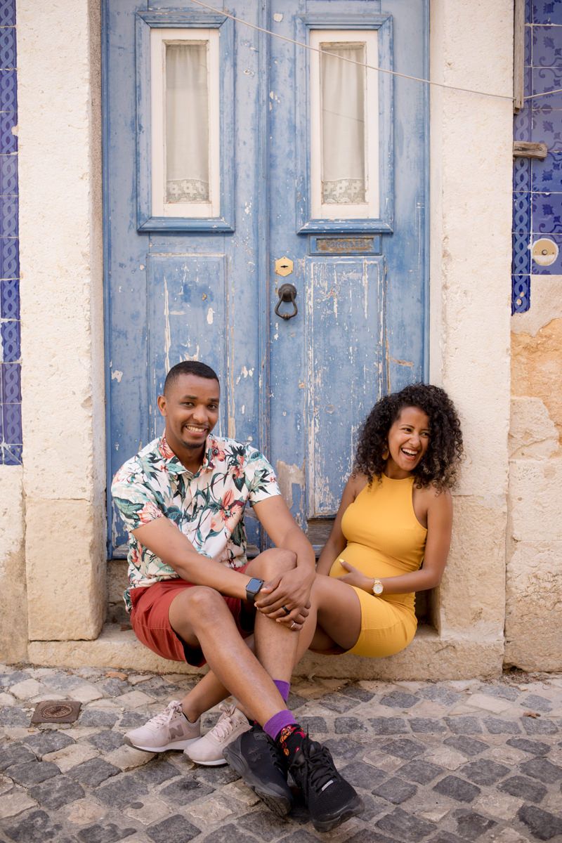 Joyful couple sitting and laughing in front of a rustic blue door on cobblestones.