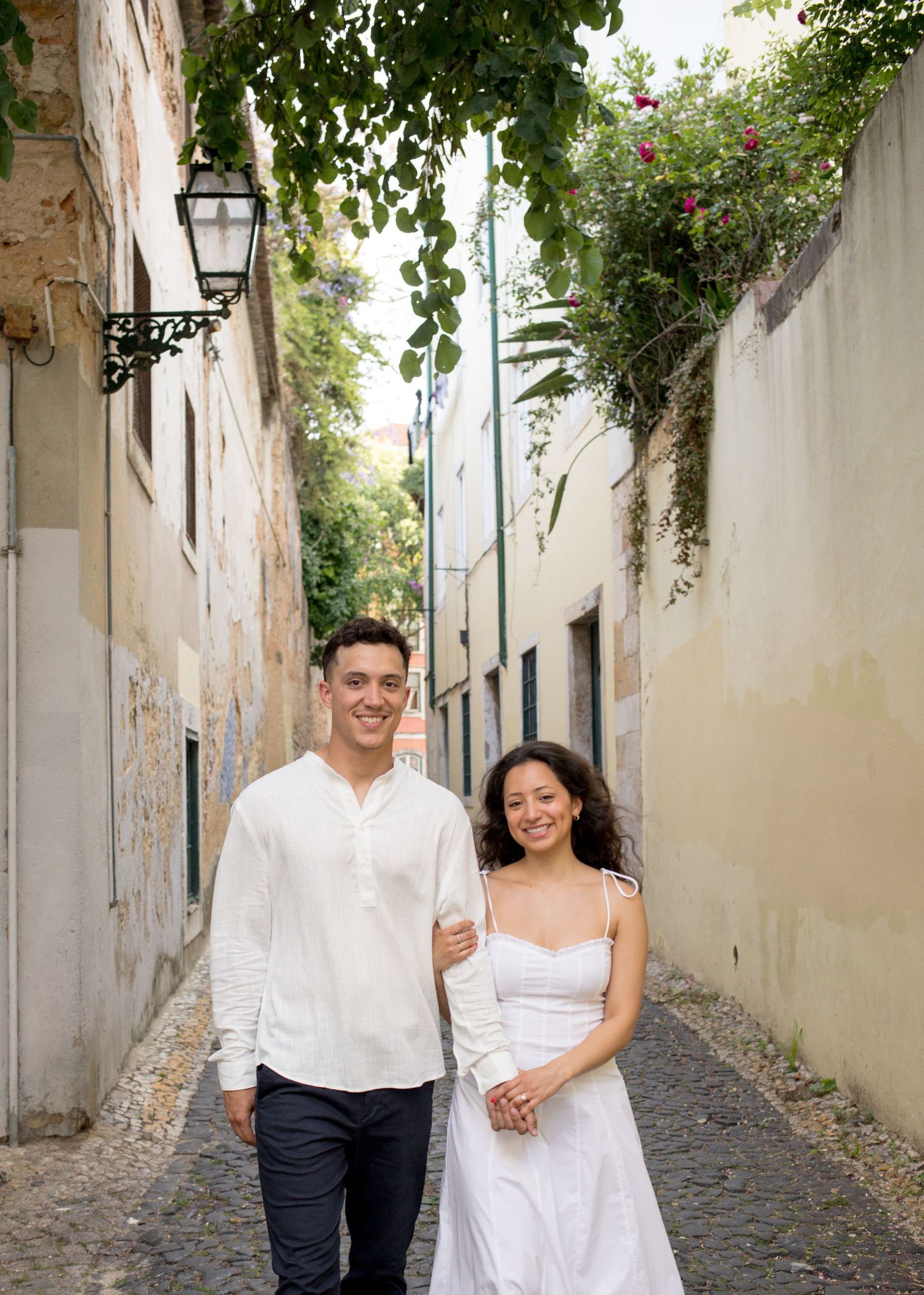 Couple walking hand in hand through a charming cobblestone alley in Lisbon, Portugal, dressed in white.