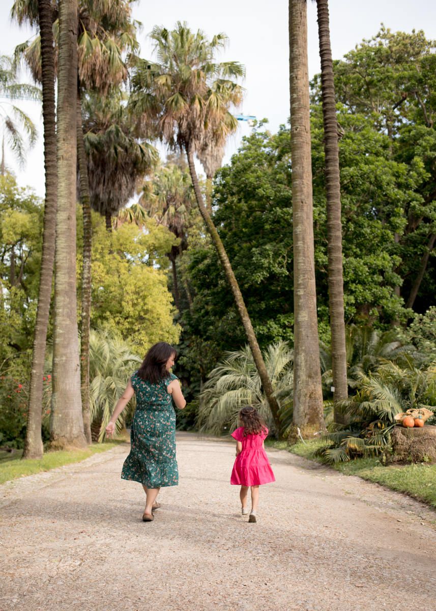A woman in a green dress and young girl in pink walk away on a palm-lined garden path.