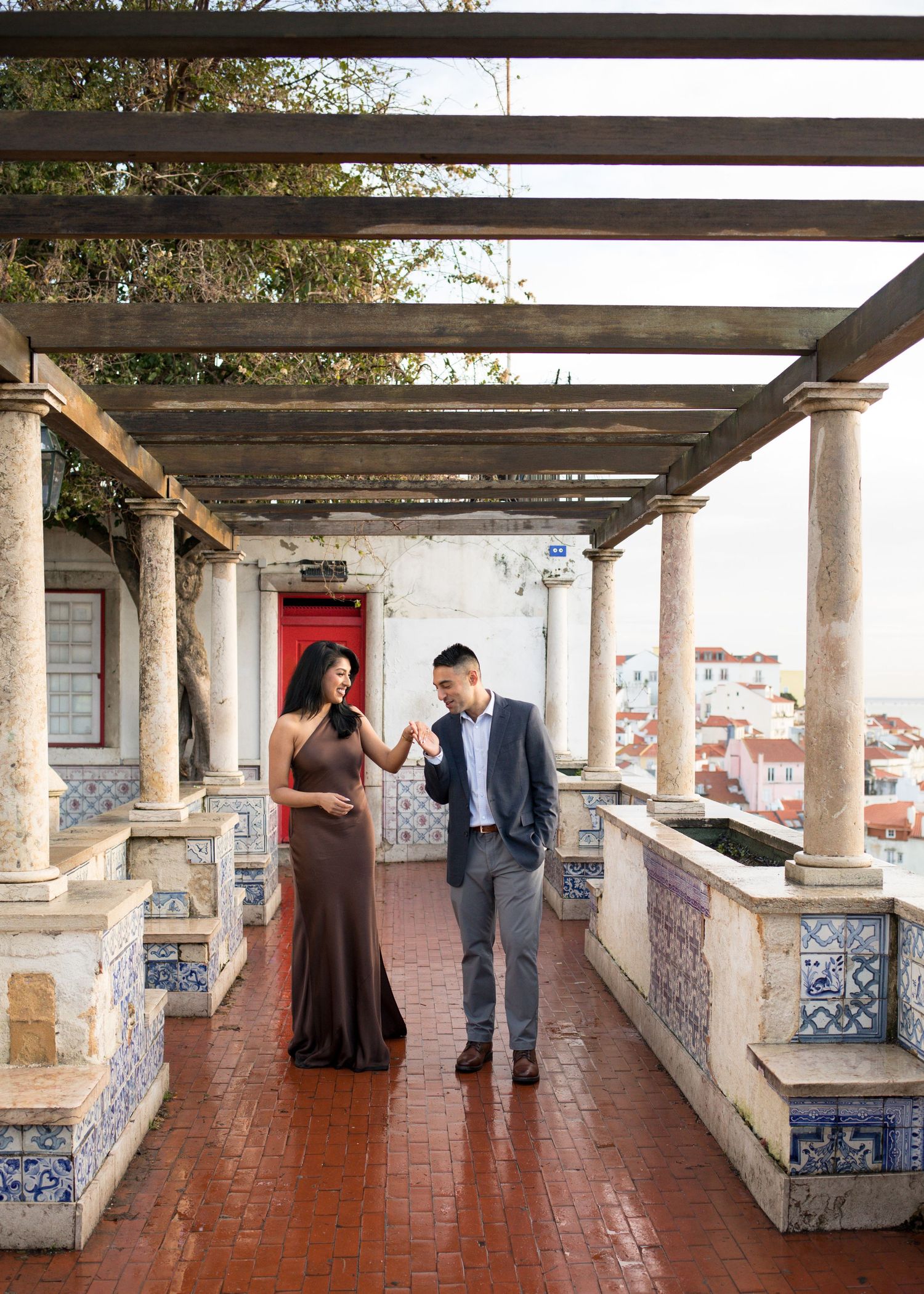 Couple walking under a pergola on a tiled terrace in Lisbon, Portugal, with colorful azulejo tiles and city views.