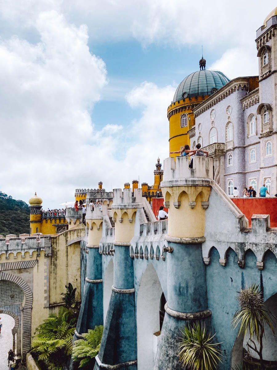 Colorful Pena Palace in Sintra, Portugal, featuring blue turrets, yellow and red towers under a partly cloudy sky.