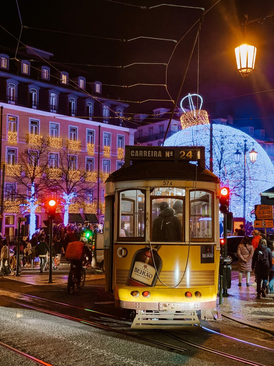 Yellow tram 24 on a festive night street in Lisbon, Portugal, with holiday lights and a glowing building backdrop.