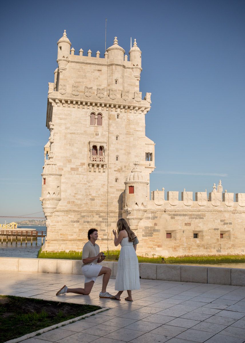 Man proposes to woman on one knee in front of the iconic Torre de Belem tower in Lisbon, Portugal.