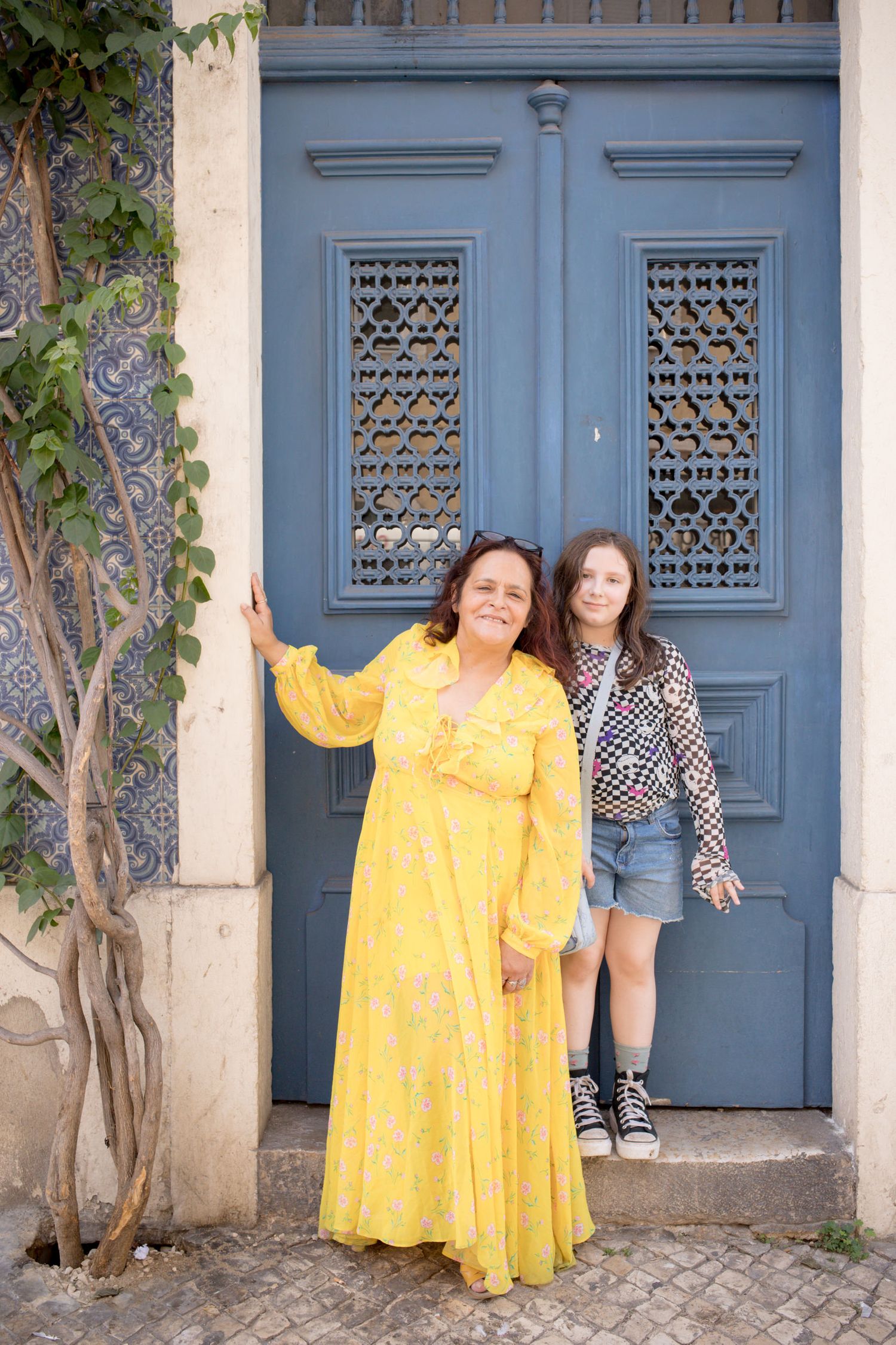 Woman in yellow dress and young girl posing before an ornate blue door in Lisbon, Portugal.