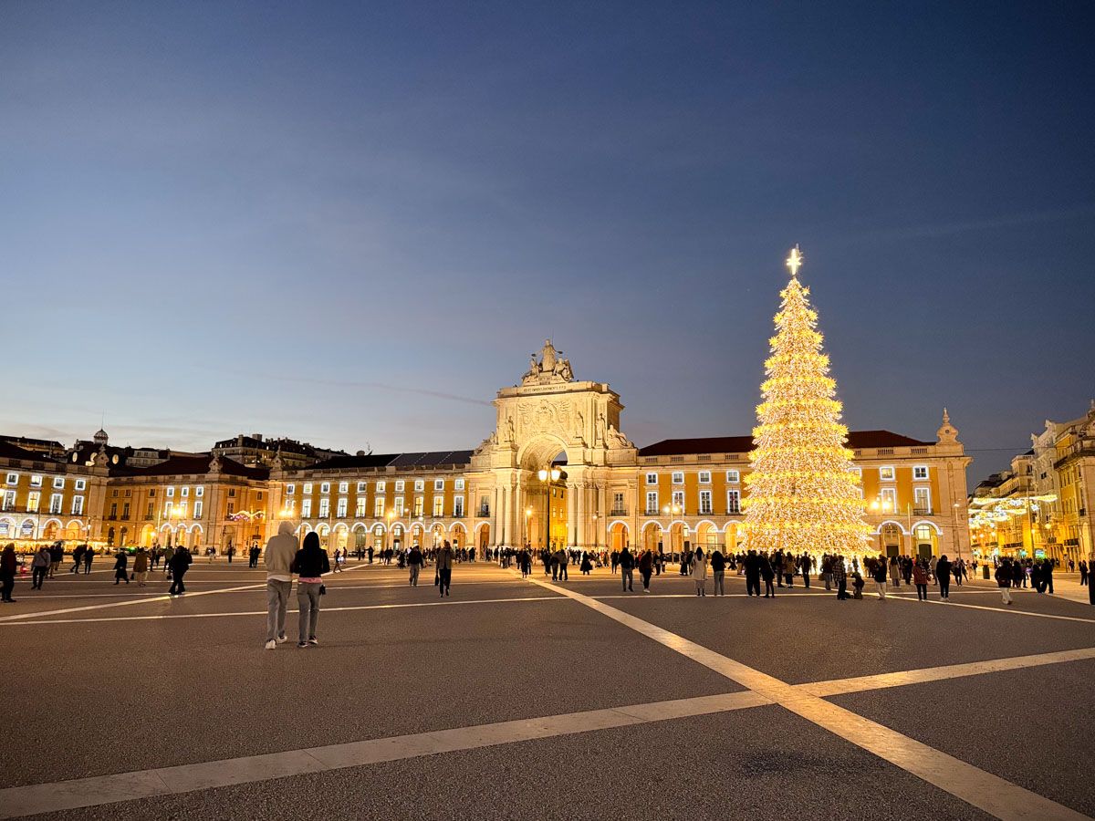Praça do Comércio in Lisbon lit up at Christmas with a glowing tree and the iconic Rua Augusta Arch at dusk.