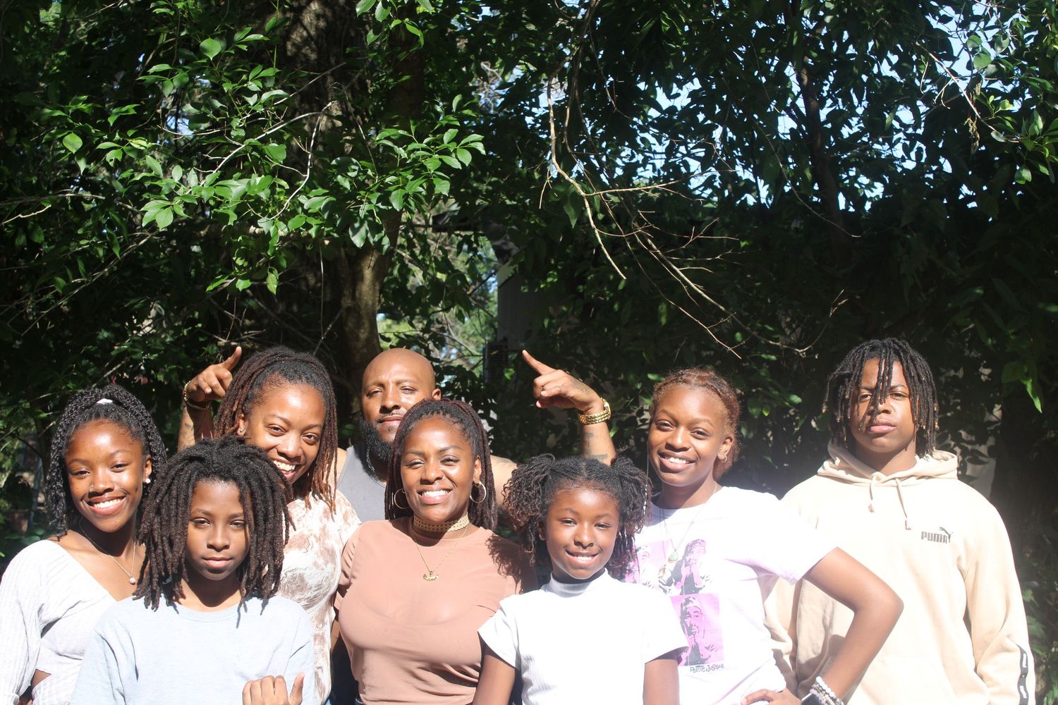 Group of young girls and a woman smiling together outdoors under a tree.