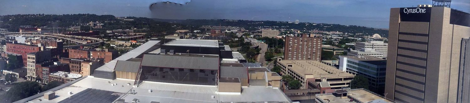 Panoramic aerial view of a mid-sized city skyline with commercial buildings, roads, and urban infrastructure under a cloudy sky.