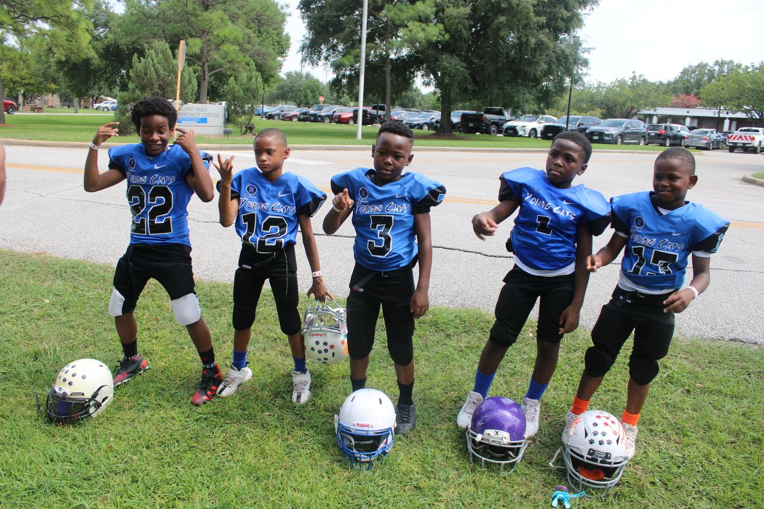 Five young boys in blue football uniforms posing together with helmets on grass field.