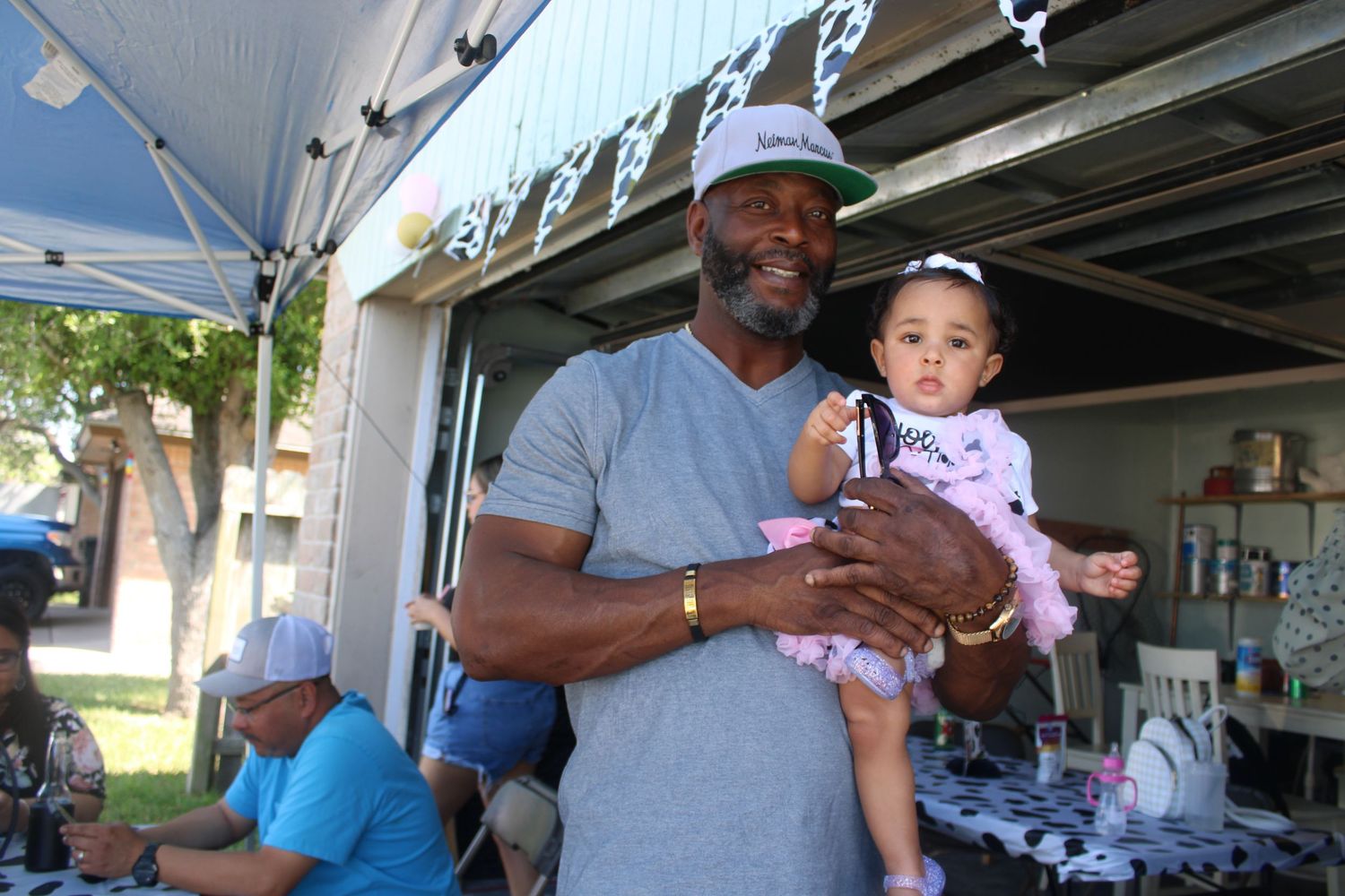 A man holding a baby girl at an outdoor party under a tent with cow print decorations.