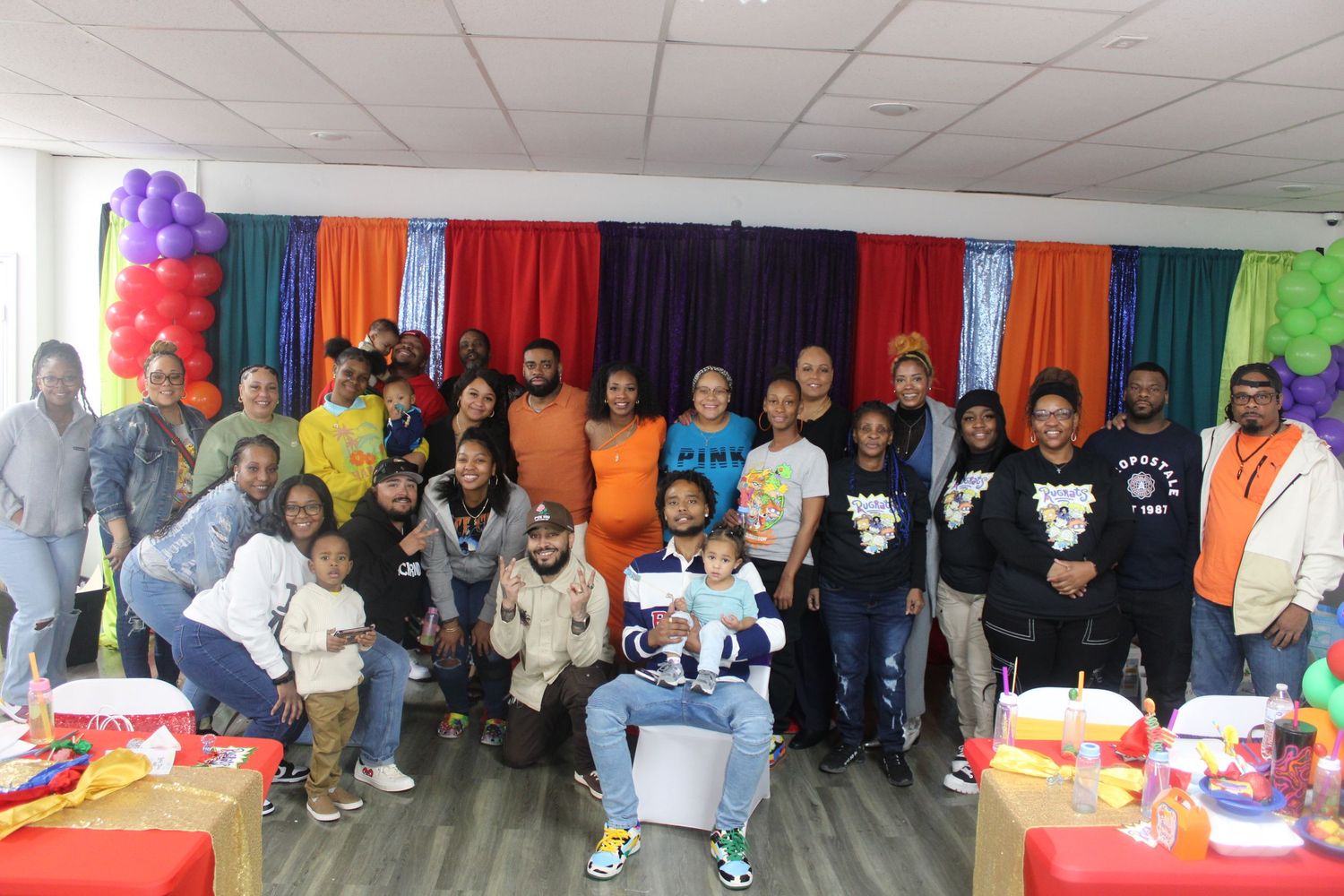 Large diverse family group posing together at a colorful balloon-decorated celebration party.