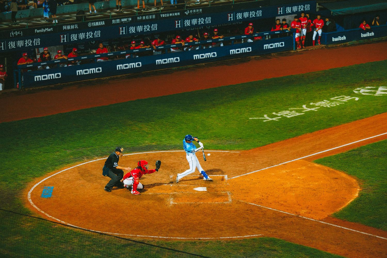 Baseball batter in blue uniform swings at a pitch during a professional game with Chinese advertising boards.