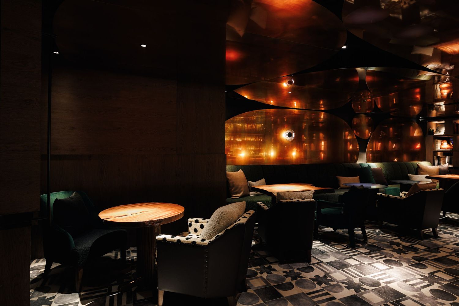 Moody upscale lounge seating area with velvet chairs and warm ambient copper wall lighting.