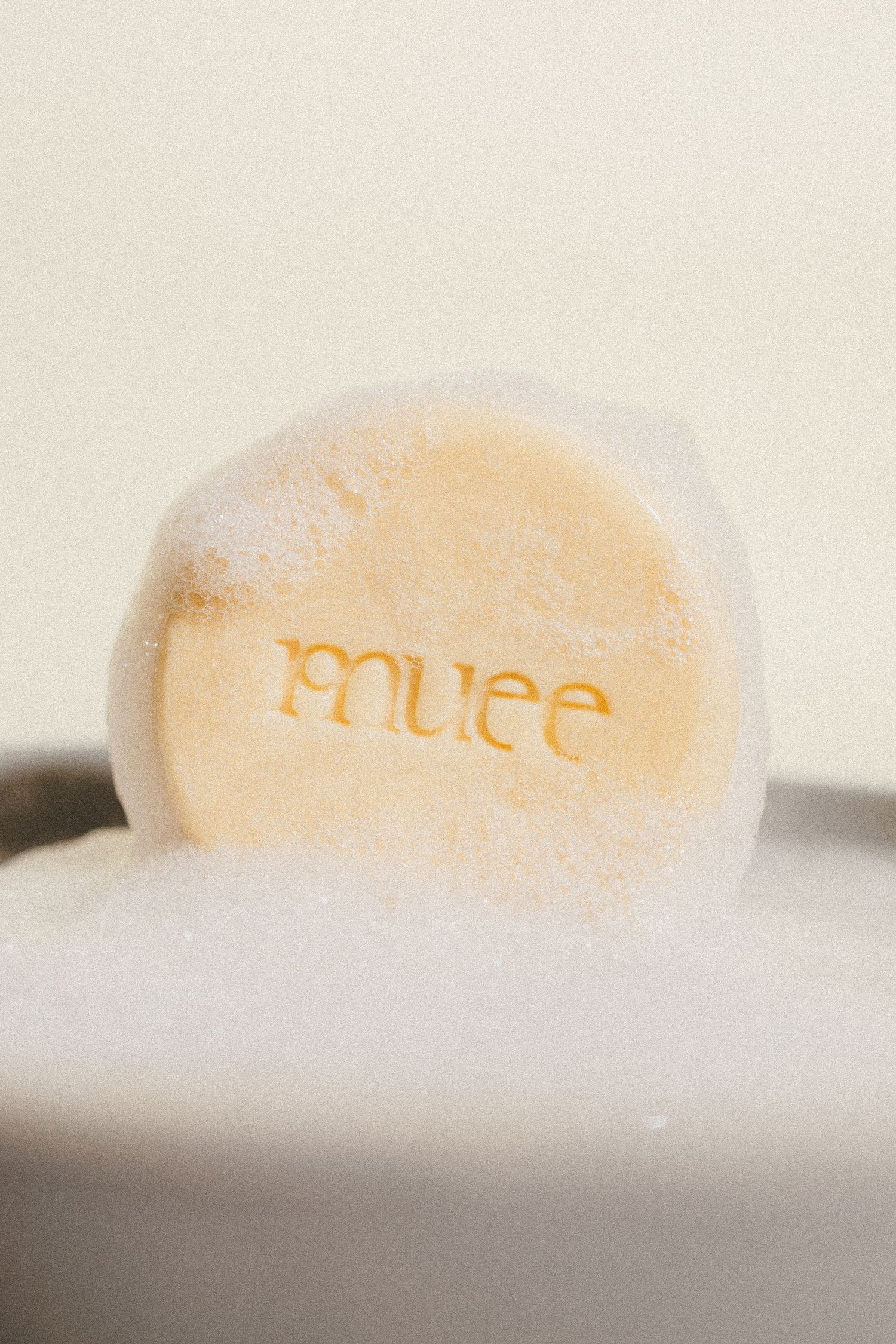 Close-up of a Muee branded round soap bar covered in white lather foam.