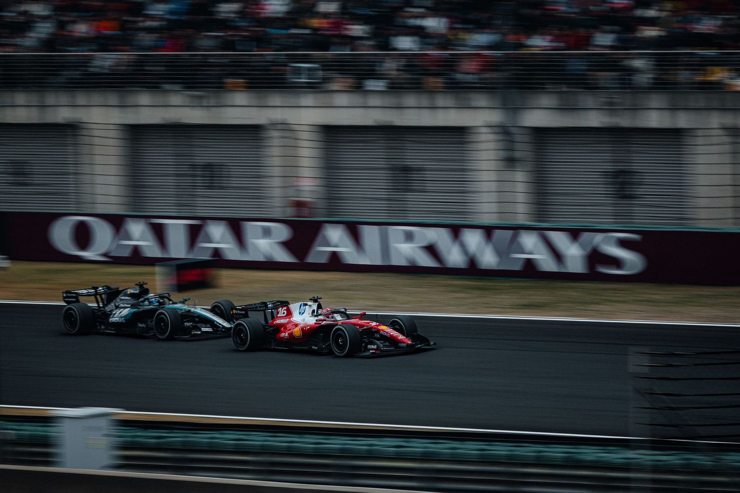 Two F1 cars racing on track with Qatar Airways sponsor banner visible in background.