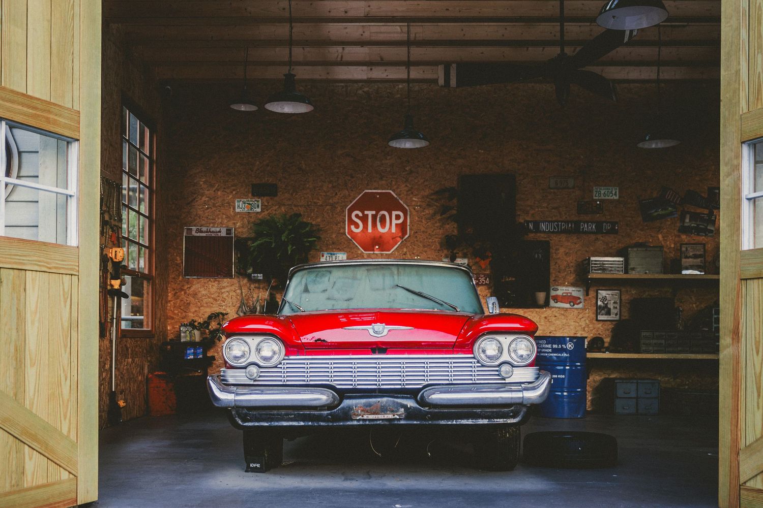 A classic red vintage car parked inside a rustic garage with a stop sign on the brick wall.