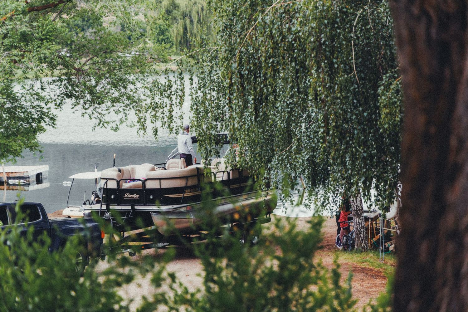 Peaceful lakeside scene with a pontoon boat docked under weeping willow trees in summer.