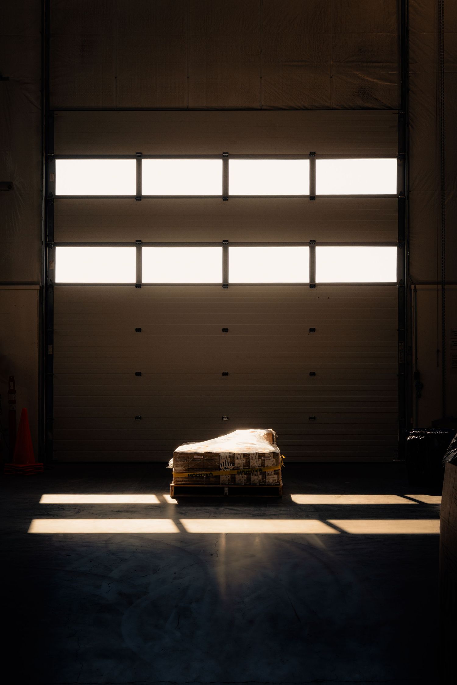 A wooden pallet illuminated by sunlight streaming through a large industrial garage door.
