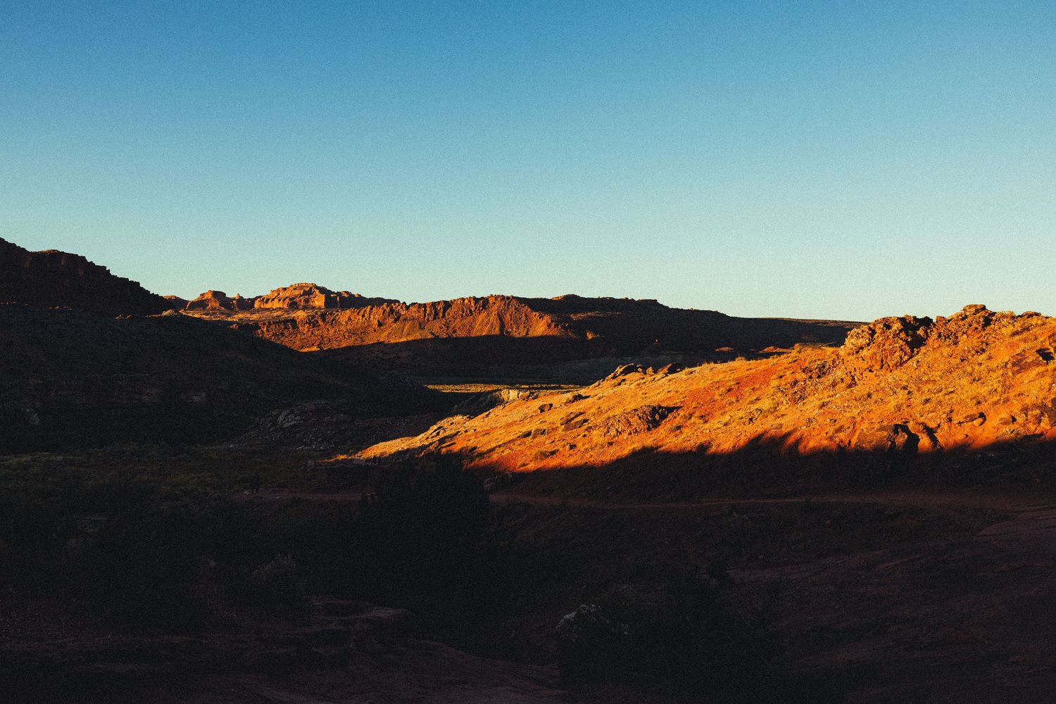 Golden hour sunlight illuminating rugged desert canyon landscape with warm red hues.