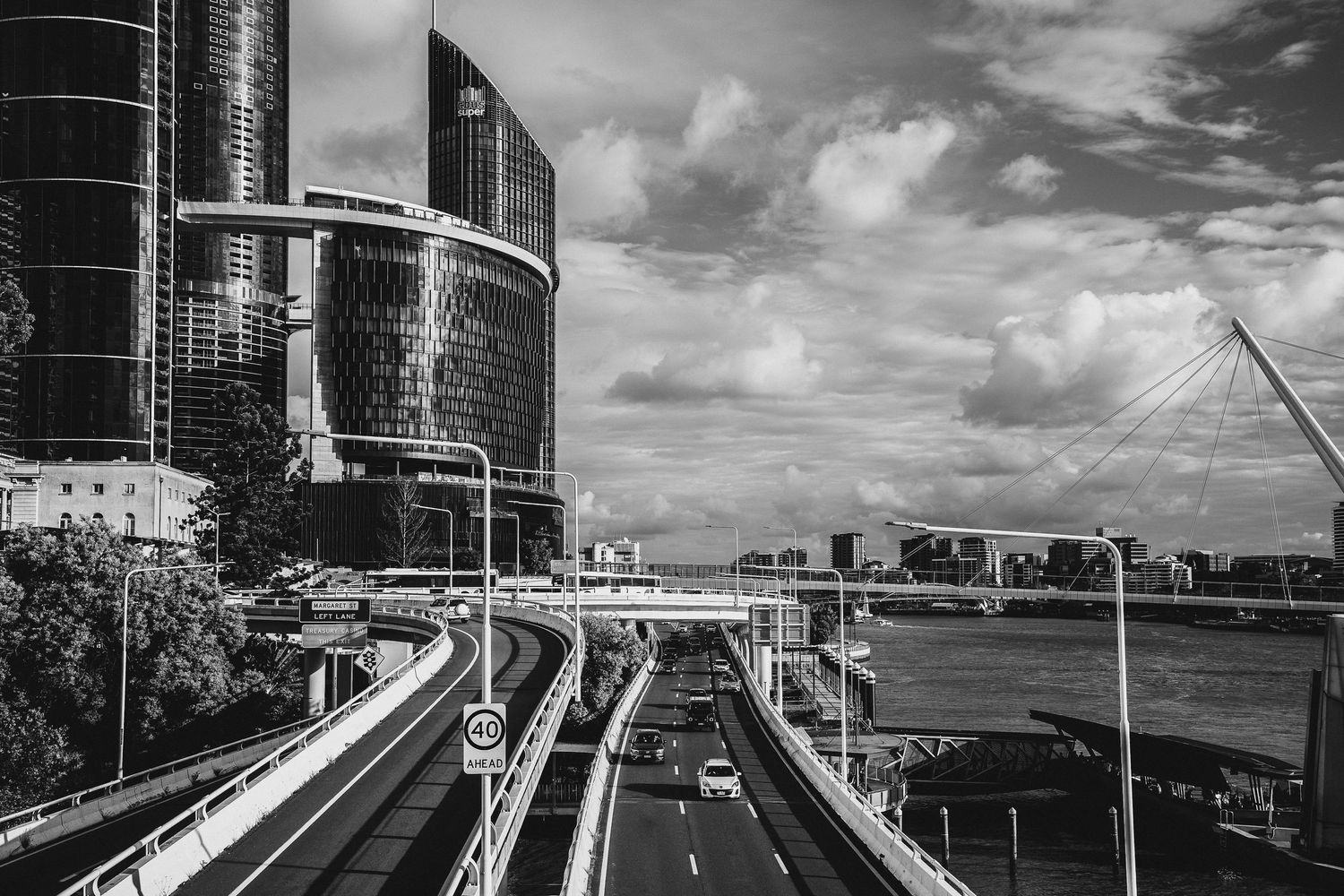 Black and white cityscape featuring modern skyscrapers, elevated highway, and bridge over a river.