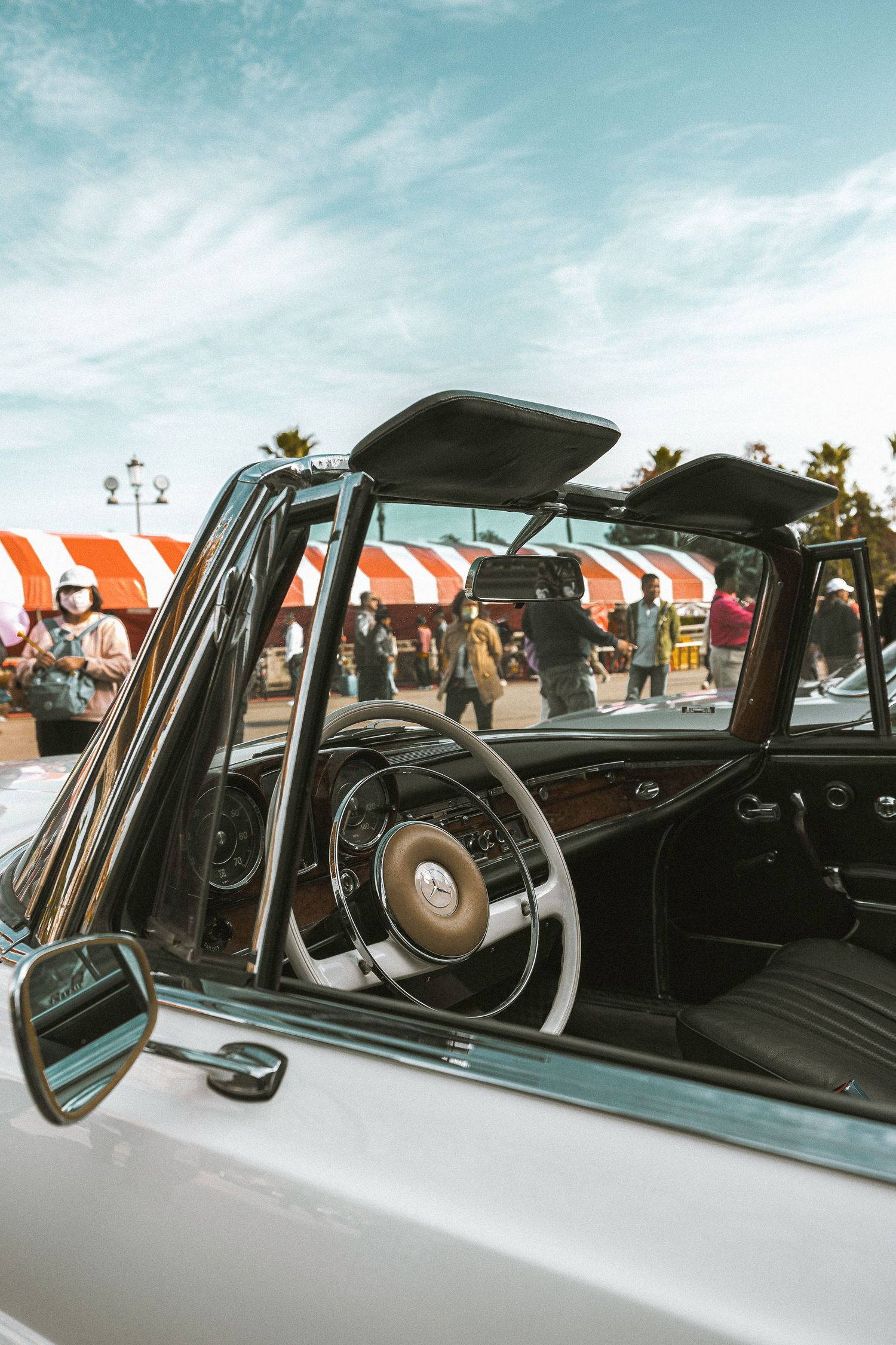Interior view of classic white Mercedes-Benz convertible with wood dashboard and white steering wheel.