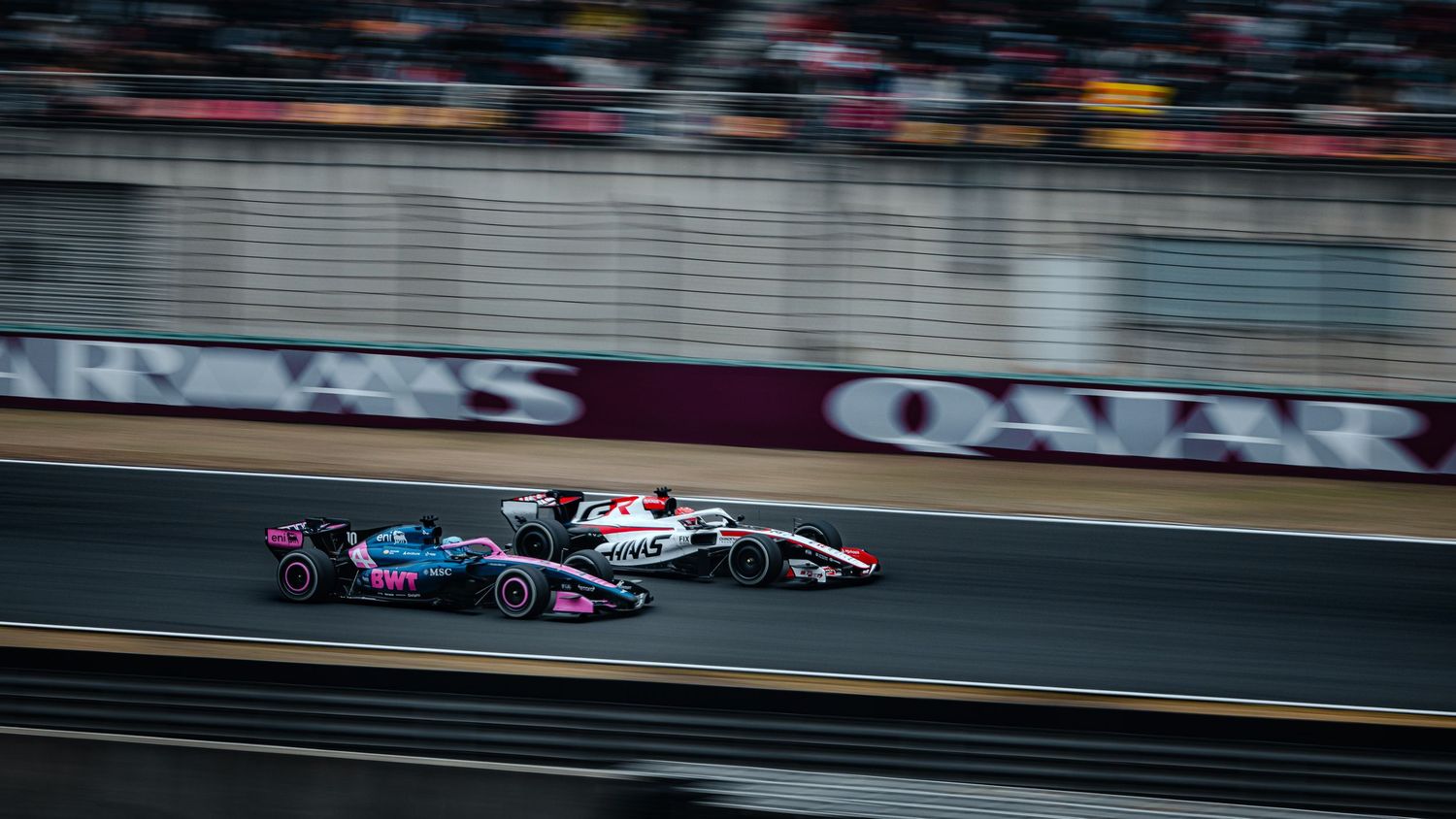 Two Formula 1 cars racing side by side past Qatar Airways advertising boards on circuit.