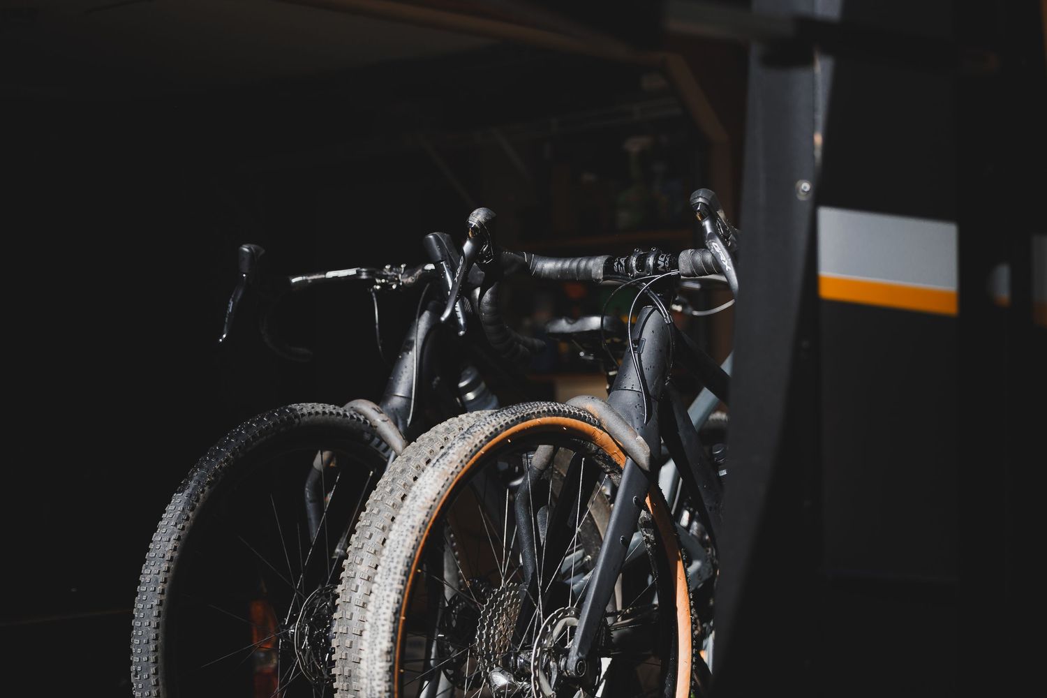 Dark moody garage scene featuring two mountain bikes with knobby tires parked in shadow.