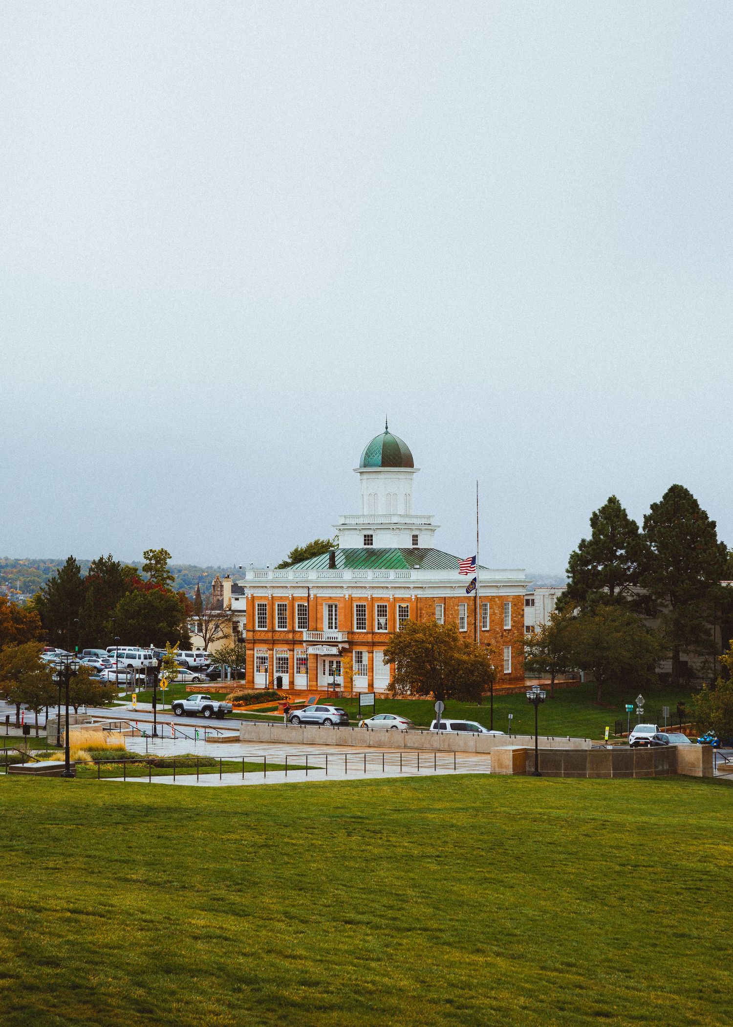 Historic red brick courthouse with green dome on grassy hill on overcast day.