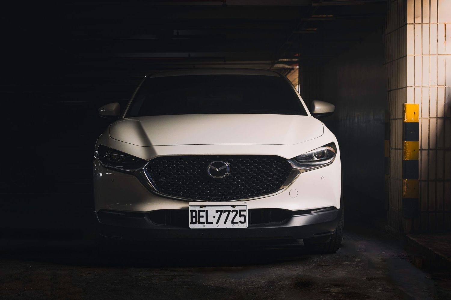 White Mazda CX-30 parked in dark underground garage facing forward with license plate BEL-7725.