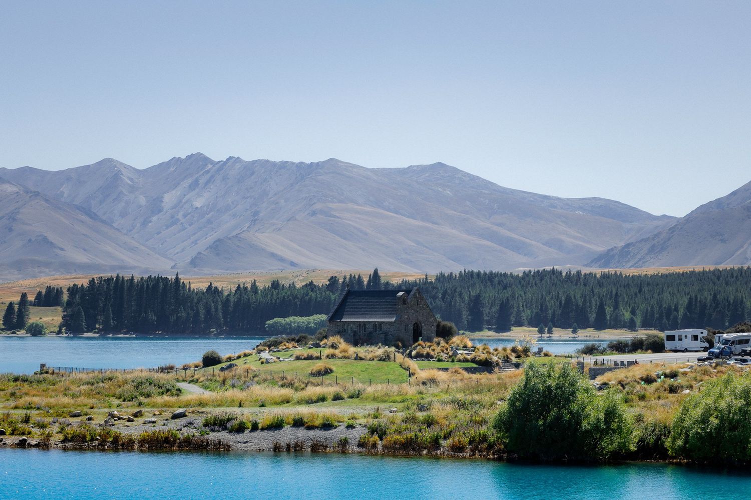 The Church of the Good Shepherd sits beside the vivid turquoise waters of Lake Tekapo with mountains behind.