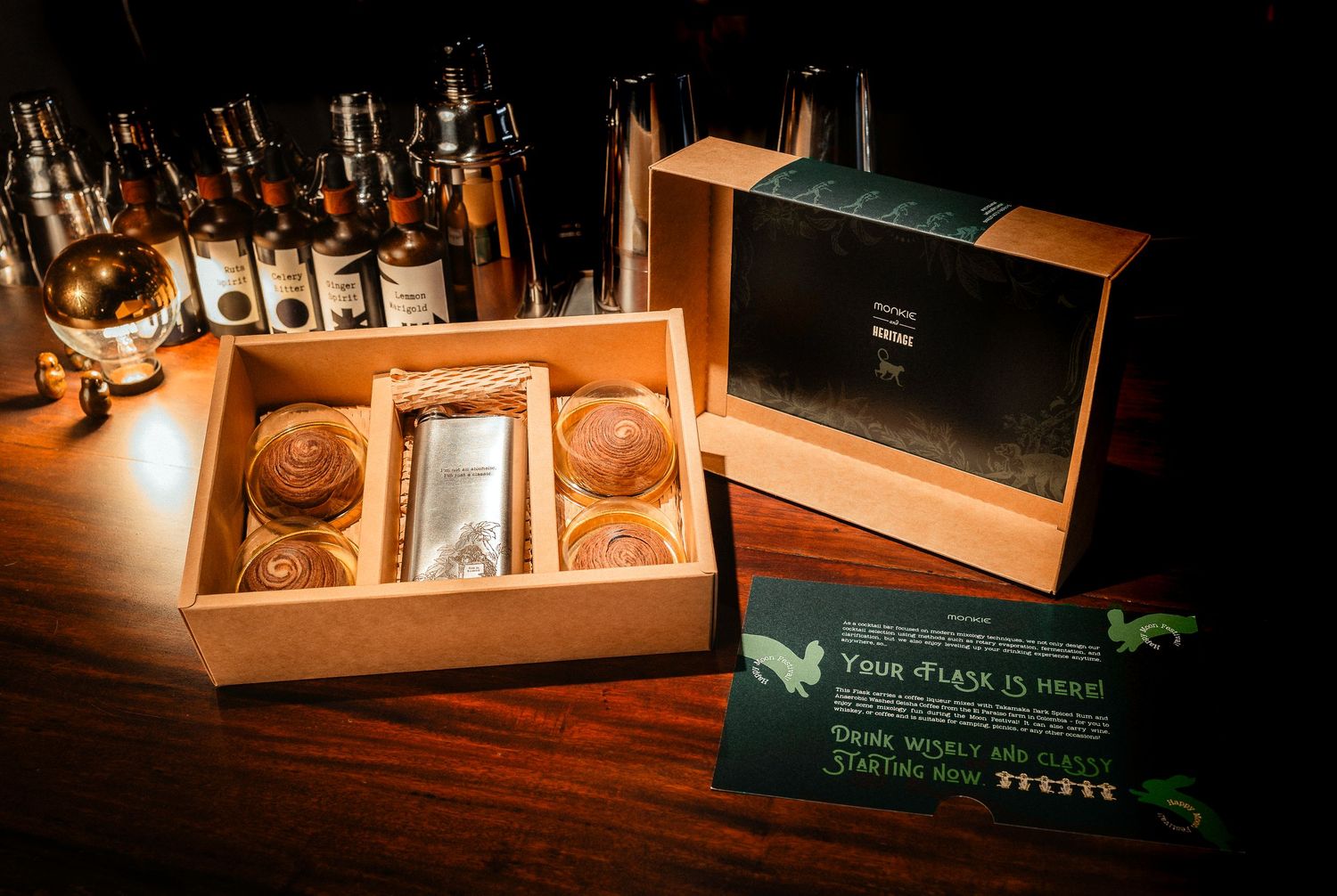 Luxury whisky gift box set with two glasses and bottle on wooden bar counter with green invitation card.