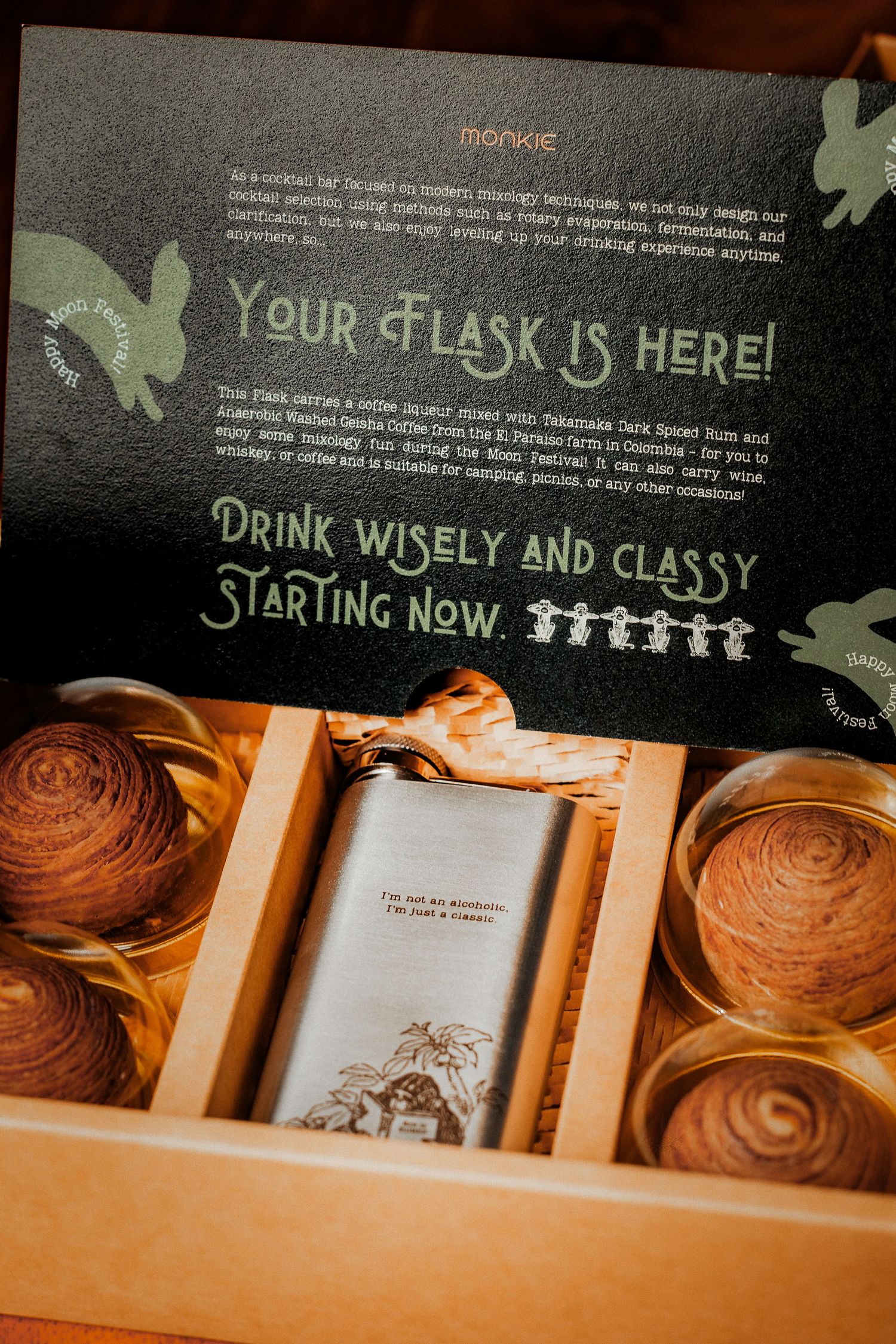 Gift box containing an engraved hip flask with cinnamon rolls and text reading Your Flask Is Here, Drink Wisely and Classy.