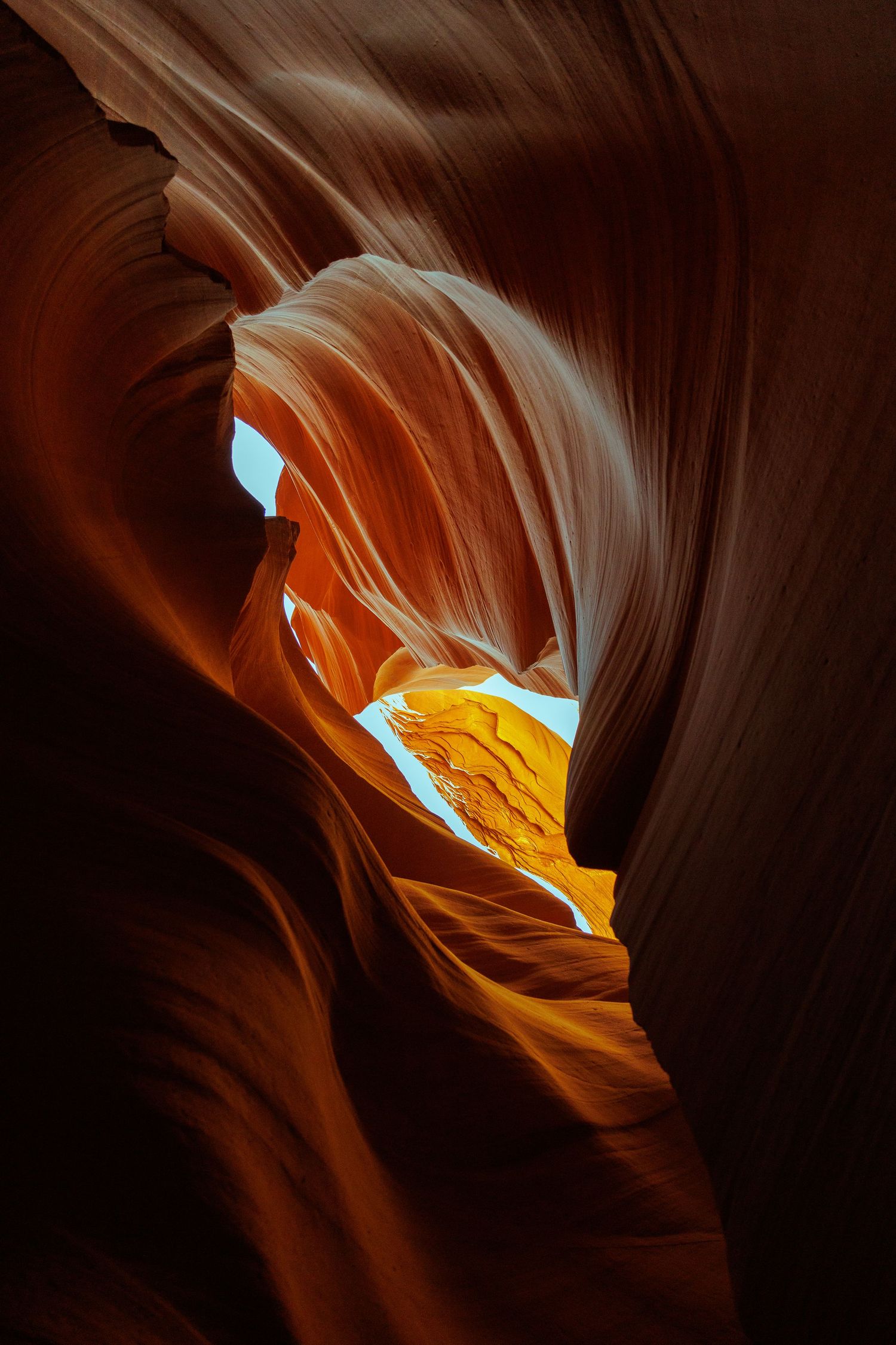 Stunning Antelope Canyon slot canyon with glowing orange sandstone walls and narrow opening revealing blue sky above.