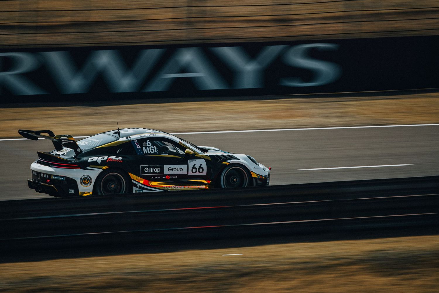 Black Porsche GT3 race car number 66 speeding along racing circuit with blurred background.