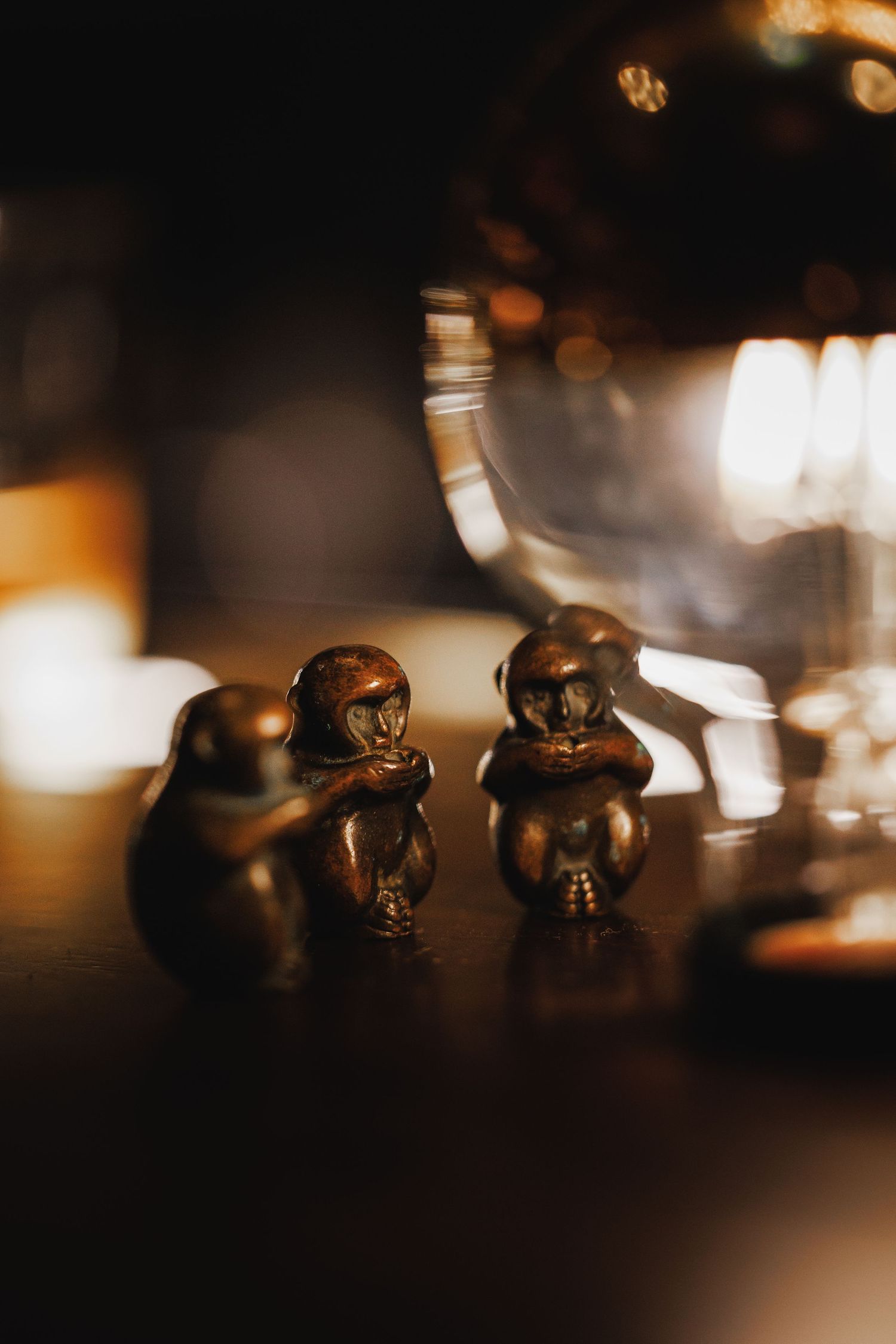 Two small bronze monkey figurines sitting together on a dark surface with warm bokeh lighting.