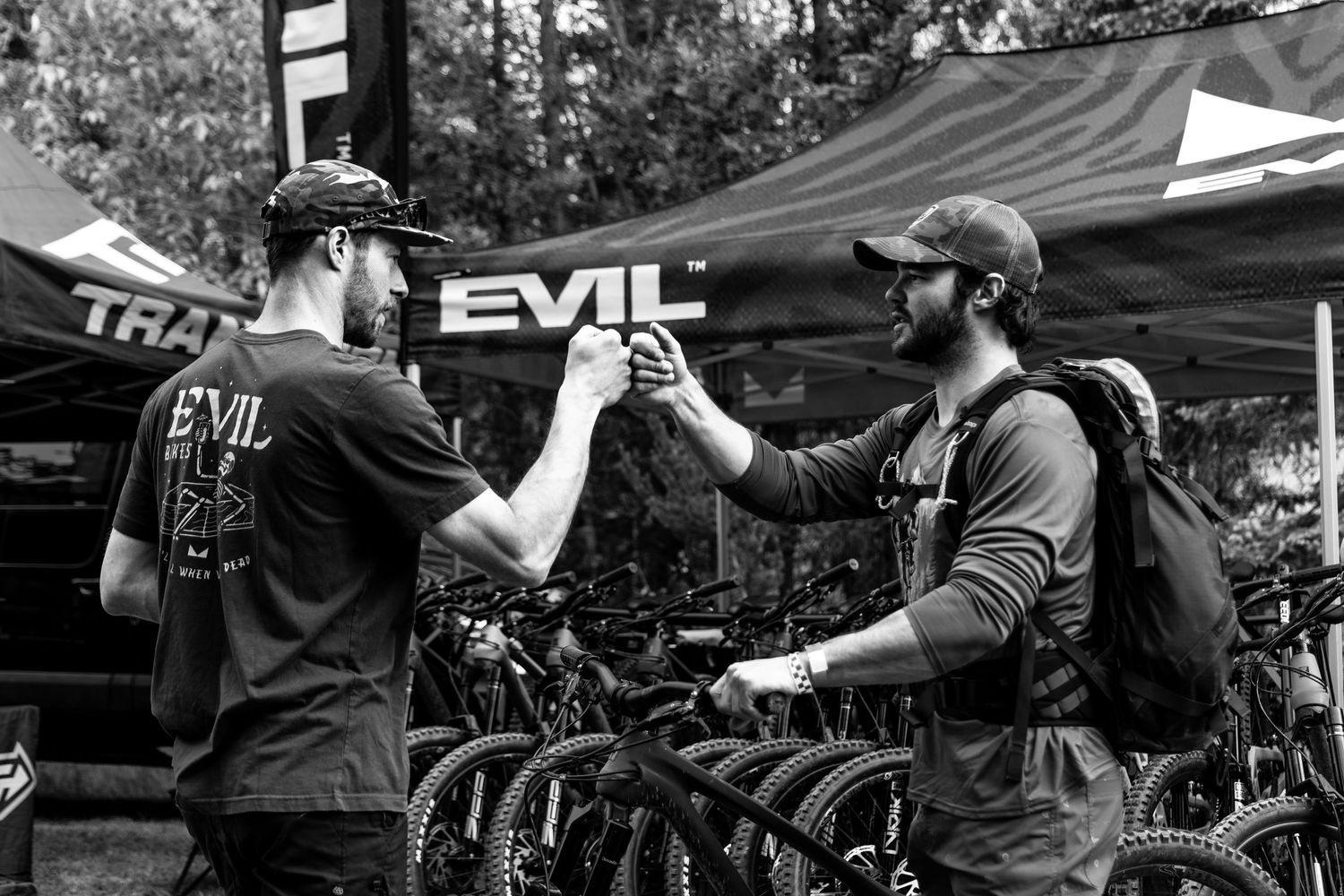 Black and white photo of two mountain bikers fist bumping at Evil Bikes demo event.