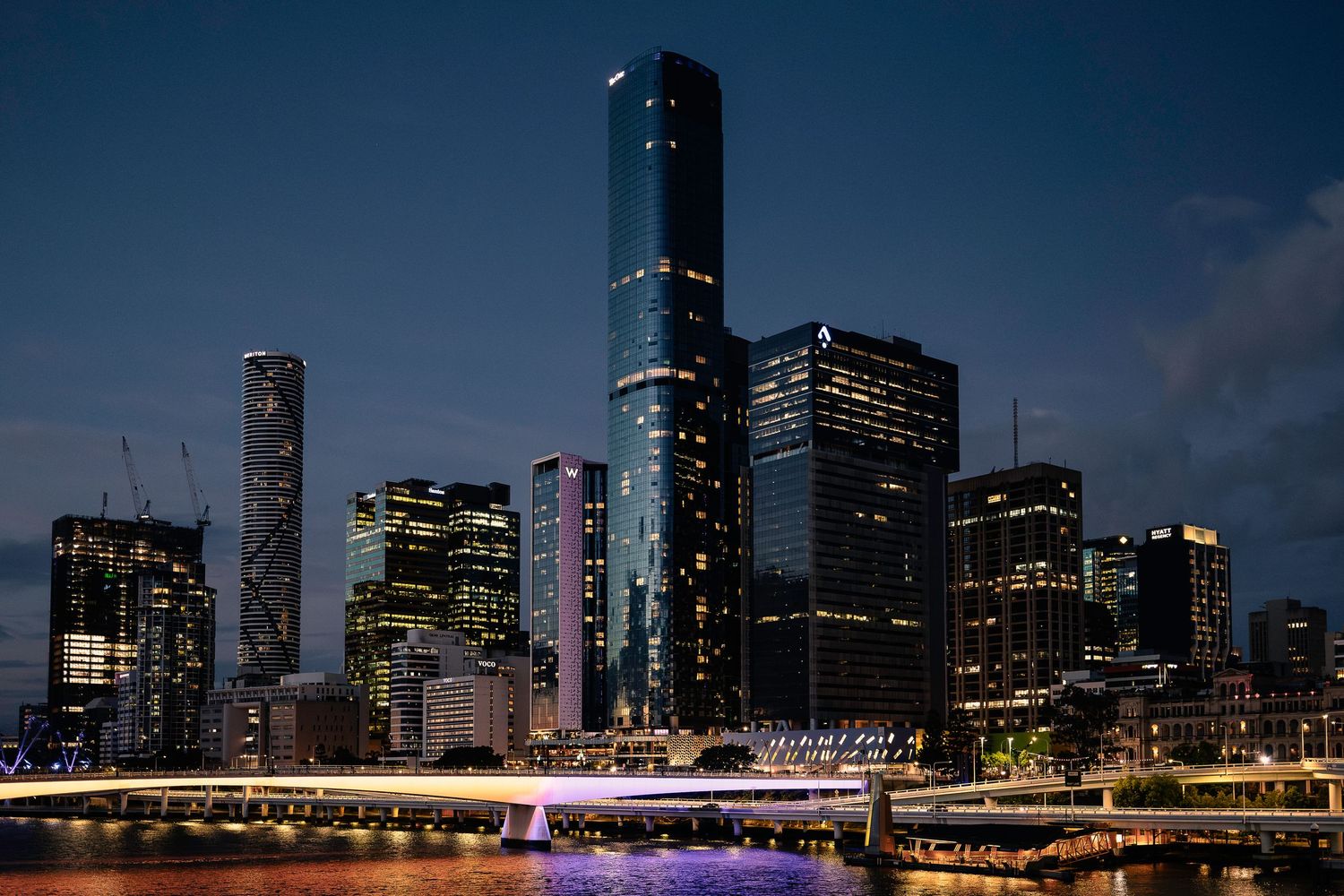 Brisbane city skyline illuminated at night reflecting on river with bridge light trails.