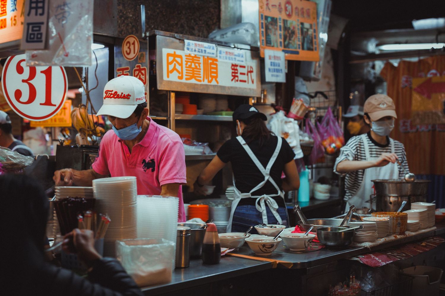 Busy Taiwanese night market food stall with workers in pink shirts and aprons preparing meals.
