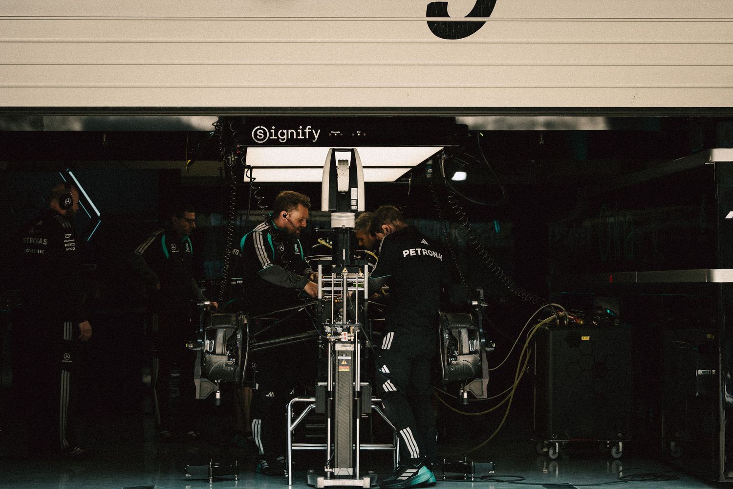 Mercedes F1 pit crew mechanics working on race car in garage under Petronas sponsorship.