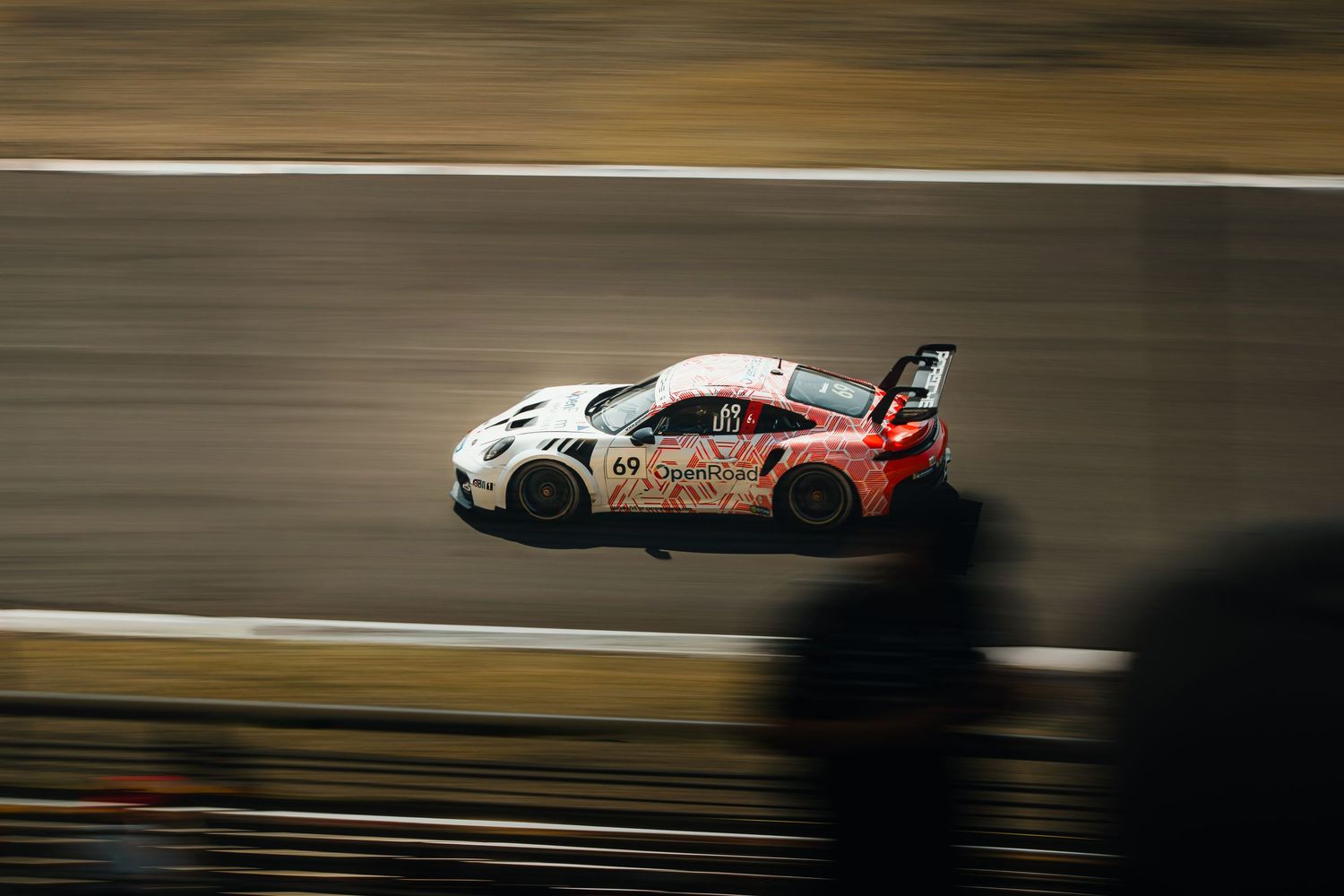 White Porsche GT3 race car with pink livery speeding on track with motion blur effect.