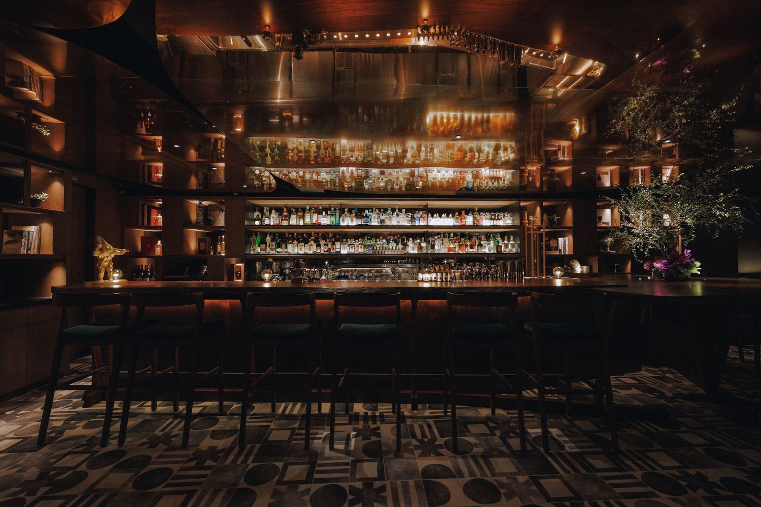 Elegant dark cocktail bar interior with backlit shelves of spirits and leather bar stools.