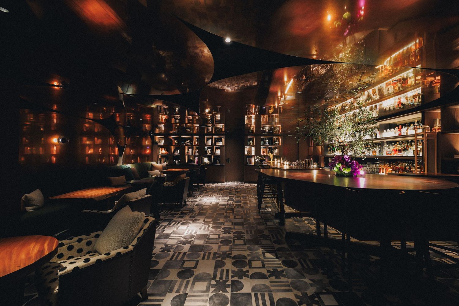 Sophisticated dimly lit cocktail bar with patterned floor, plush seating and illuminated bottle display.