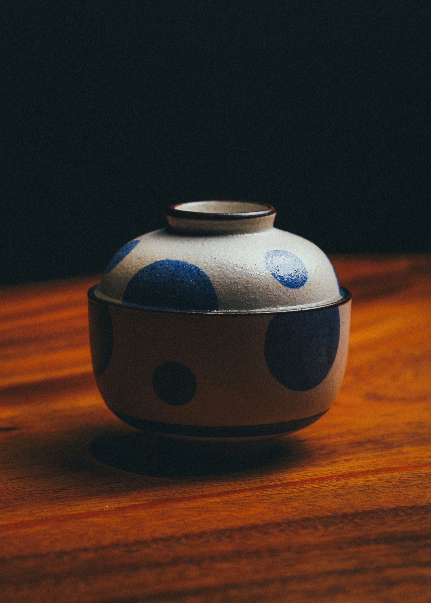 Japanese ceramic bowl with blue polka dot pattern and lid on a wooden surface.
