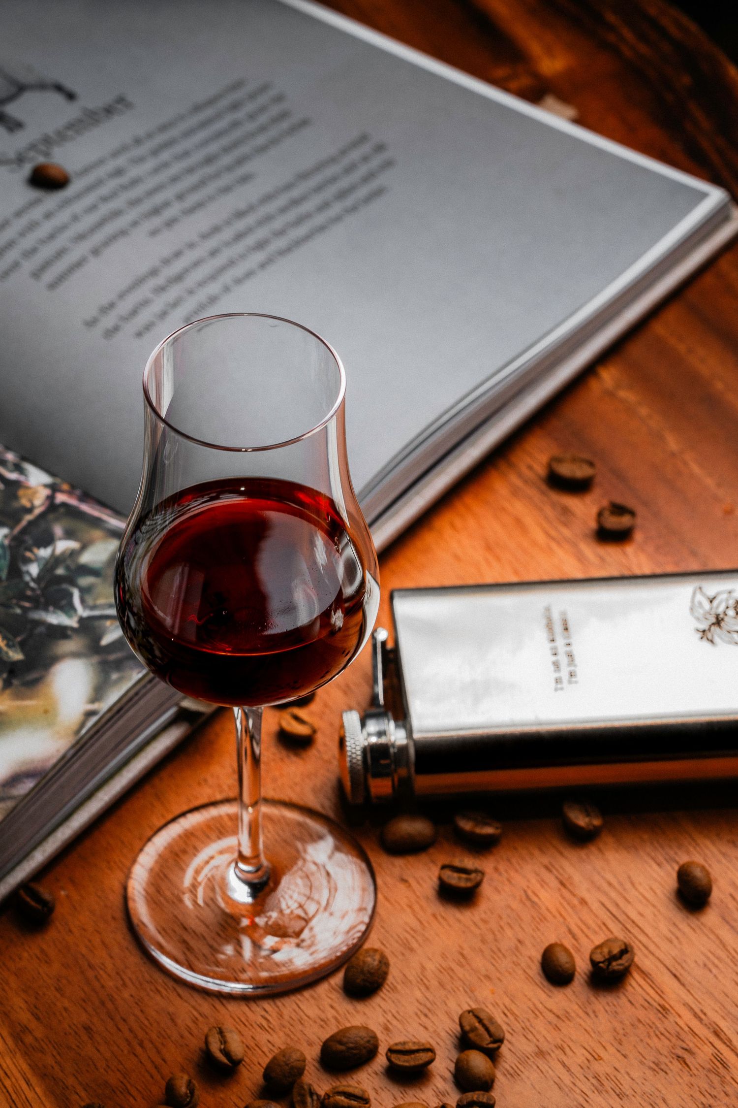 Elegant wine glass filled with red wine beside a flask and scattered coffee beans on a wooden surface.