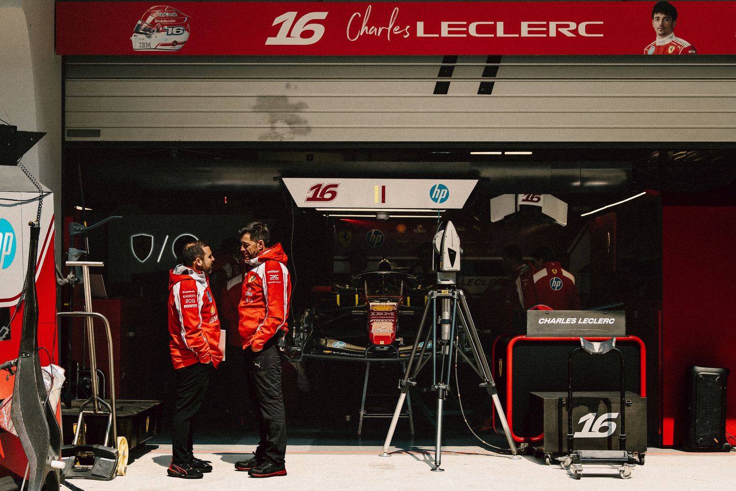 Charles Leclerc Ferrari Formula 1 team garage pit lane with mechanics and equipment at race circuit.