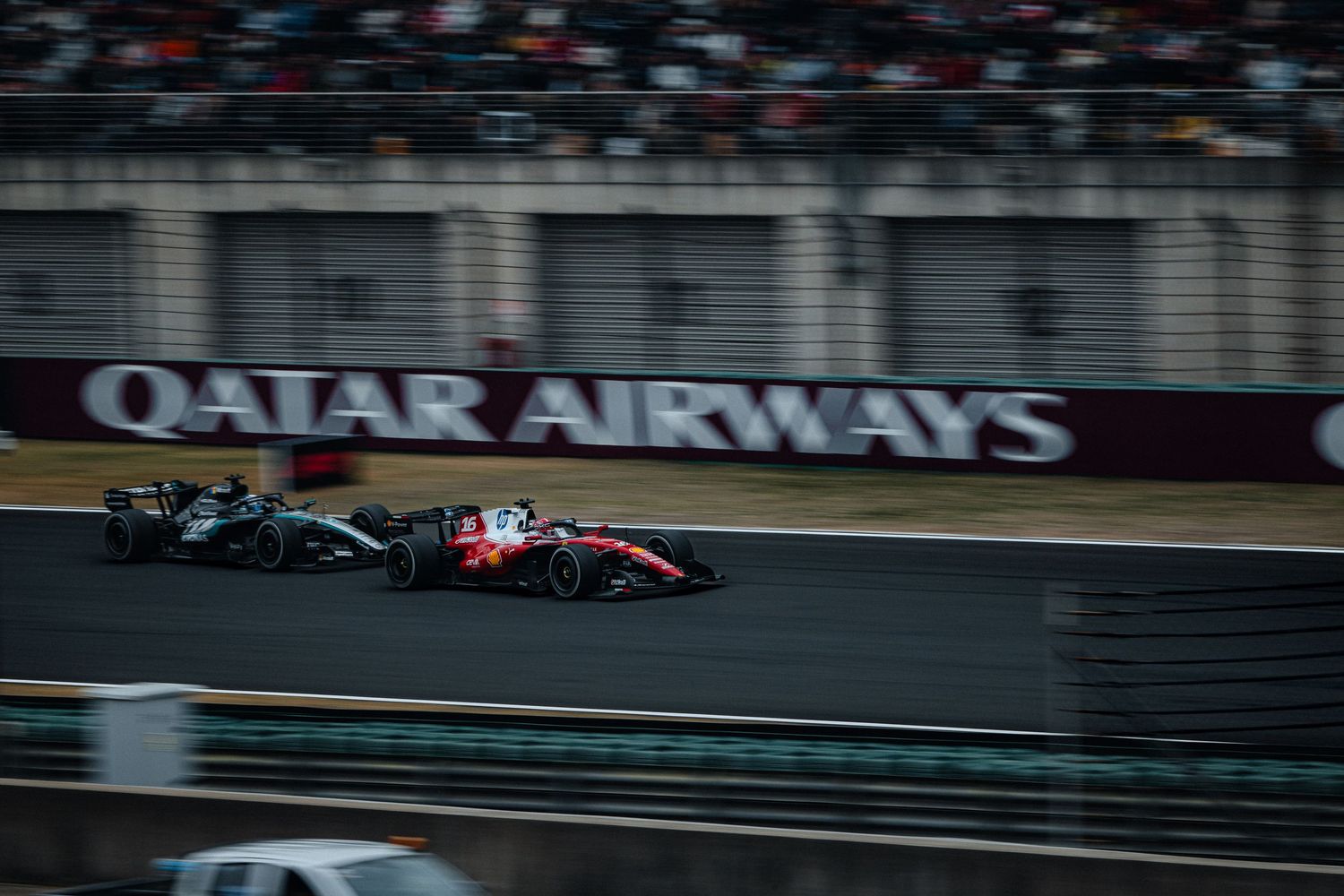 Two Formula 1 cars racing on track with Qatar Airways advertisement banner in background.