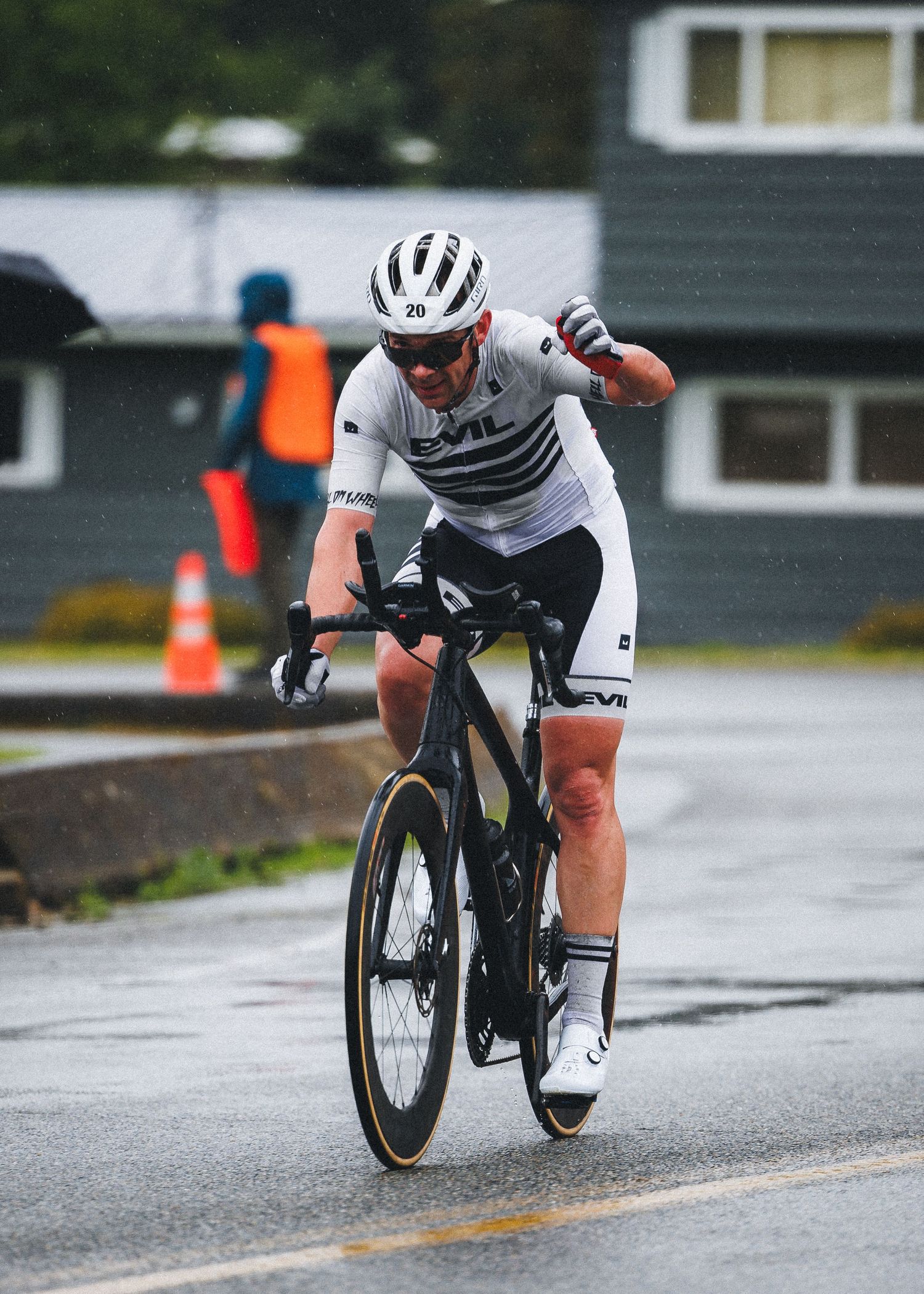 Cyclist in white Evil kit and helmet races in wet conditions on a road bike during a rainy criterium event.