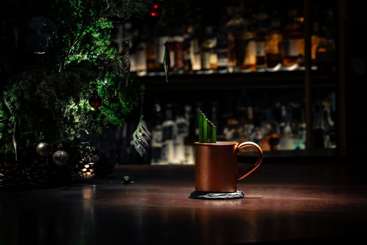 A Moscow Mule cocktail in a copper mug on a dark bar counter with a festive green garnish.