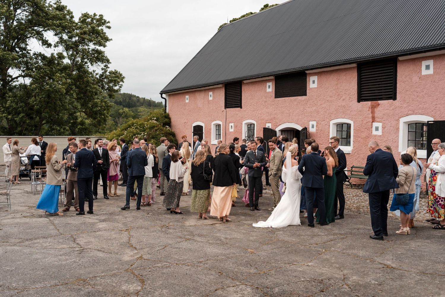 Wedding guests line up for a group photo outside a pink barn venue in the countryside.
