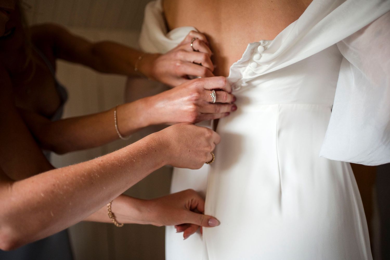 Close-up of hands helping to button up a white wedding dress during bridal preparations.