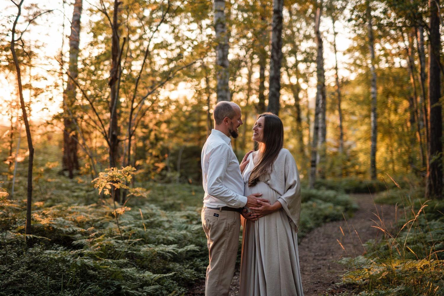 A couple embraces on a forest path during golden hour sunset as sunlight filters through autumn trees.